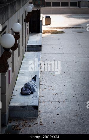 Un senzatetto dorme su una panchina di pietra di fronte a un edificio vicino al centro di Nashville, Tennessee. Foto Stock