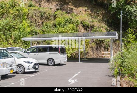 Una stazione di ricarica coperta per veicoli elettrici con pannelli solari sul tetto in un parcheggio dell'hotel pieno di veicoli con motore a combustione in una calda estate Foto Stock