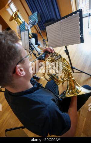 Musicista che suona il corno francese mentre guarda gli spartiti durante la pratica della band filarmonica Foto Stock