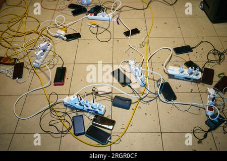 Pavimento pieno di prese multiple, cavi elettrici, cavi e telefoni di ricarica Foto Stock