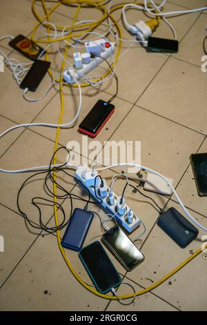 Pavimento pieno di prese multiple, cavi elettrici, cavi e telefoni di ricarica Foto Stock