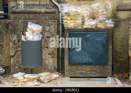 Contenitori monouso per alimenti in plastica impilati accanto a una tanica di raccolta rifiuti Foto Stock