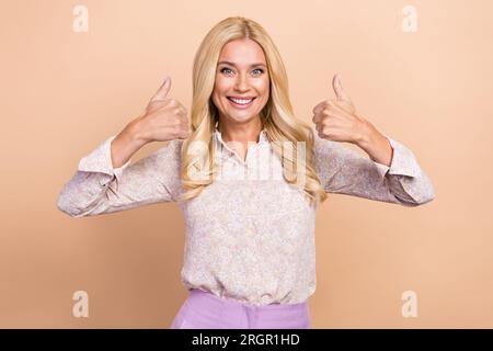 Ritratto di un'attraente lavoratrice d'ufficio che indossa una camicia da ufficio elegante e informale che solleva i pollici su uno sfondo isolato di colore pastello beige Foto Stock