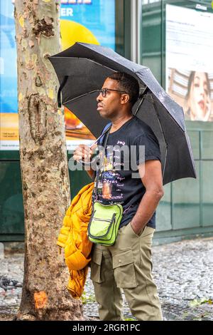 Uomo nero che si rifugia sotto ombrello nella piovosa Parigi, Francia. Foto Stock