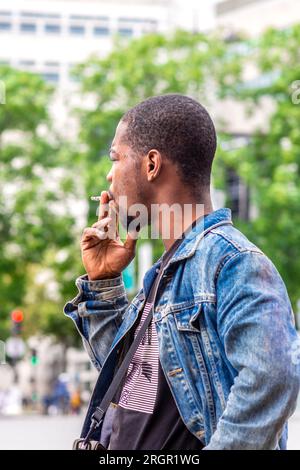 Giovane uomo nero in giacca di denim che fuma sigaretta - Parigi, Francia. Foto Stock