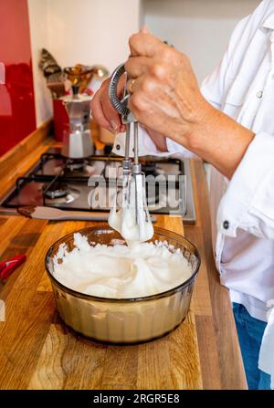 Cuoca casalinga sbattendo a mano gli albumi a punte rigide per preparare una mousse al cioccolato o una meringa Foto Stock