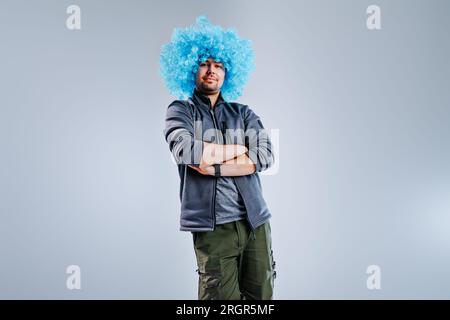 Giovane uomo che posa con una parrucca da clown blu su sfondo grigio Foto Stock