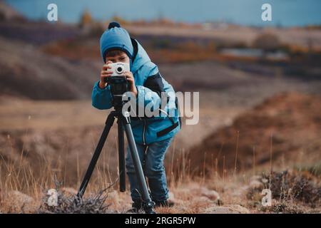 Ragazzo che scatta foto con la fotocamera sul cavalletto in montagna Foto Stock