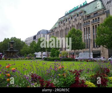 Düsseldorf, Germania - 2 agosto 2023 Una piazza chiamata Corneliusplatz con fiori, negozi e una fontana. L'edificio di fronte è Galeria Kaufhof an der Kö Foto Stock