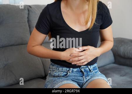 Problemi digestivi dovuti a una dieta povera. Giovane donna che soffre di forte dolore addominale mentre è seduta sul divano a casa. Foto Stock