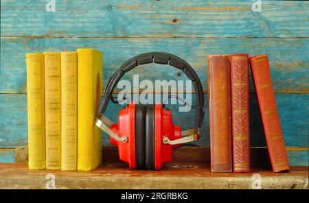 concetto di audiolibro con fila di libri e cuffie rosse vintage, tavole di legno blu sul retro Foto Stock