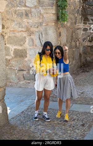 Due amiche donne che esplorano la città medievale di Toledo in Spagna utilizzando uno smartphone. I turisti utilizzano gli strumenti di navigazione per esplorare la città. Foto Stock