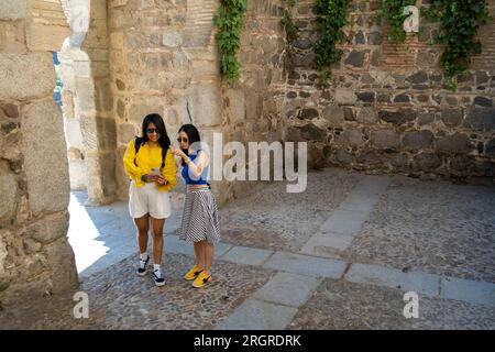 Due amiche donne che esplorano la città medievale di Toledo in Spagna utilizzando uno smartphone. I turisti utilizzano gli strumenti di navigazione per esplorare la città. Foto Stock