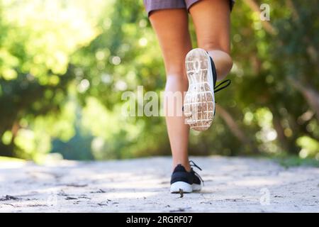 Primo piano della suola della scarpa da running mentre la donna corre su sentieri all'aperto nel parco Foto Stock