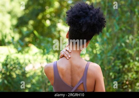 Vista posteriore di una giovane donna con il collo che sfrega afro, lesioni sportive all'aperto Foto Stock