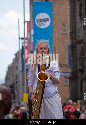 Royal Mile, Scozia, Regno Unito. 11 agosto 2023. Gli artisti di strada di High Street trovano le condizioni ventose difficili ma il clima caldo è il benvenuto con una temperatura poco superiore ai 20 gradi. La folla arriva più tardi nel corso della giornata con diverse altre piazzole per spettacoli in centro città. Nella foto: Una donna sassofonista attrae le persone dai suoi colleghi distribuendo volantini. Credito: Notizie dal vivo Archwhite/alamy. Foto Stock