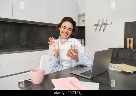 Ritratto di una giovane donna in video chat con un'amica sullo smartphone, onde mano sulla fotocamera del telefono cellulare, chiama qualcuno utilizzando l'applicazione Foto Stock