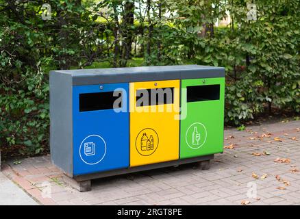 Tre diversi contenitori per la raccolta rifiuti per lo smistamento dei rifiuti nel parco. Giallo per plastica, verde per vetro, blu per carta. Separazione e smistamento dei rifiuti, co Foto Stock