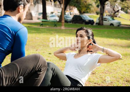 Ritratto di una donna di mezza età che fa esercizi addominali in un parco con il suo personal trainer. Concetto di sport all'aperto Foto Stock