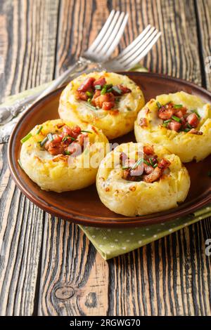 Nidi di patate cotti con purè di patate e cotti con pancetta e cipolle da vicino in un piatto sul tavolo. Verticale Foto Stock