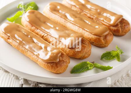 Eclair dolci francesi con ripieno di panna e ricoperti da un delicato e morbido primo piano di caramello in un piatto sul tavolo. Orizzontale Foto Stock