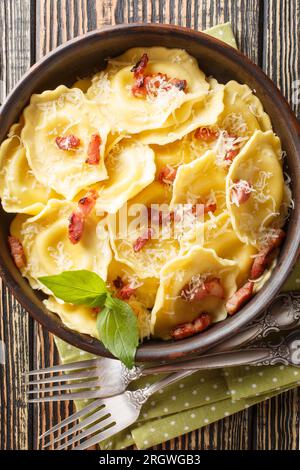 Pasta italiana a forma di girasoli girasoli farcita con formaggio, pancetta e basilico da vicino in un piatto sul tavolo. Vista dall'alto verticale Foto Stock