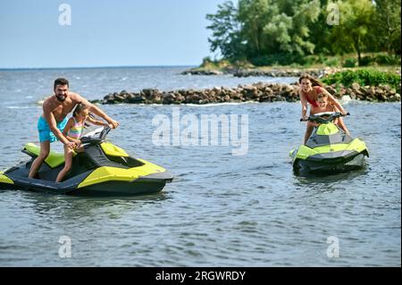 Padre, madre, figlia e figlio che corrono su moto d'acqua mentre si divertono in moto d'acqua nell'oceano. Foto Stock