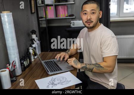 Giovane con tatuaggi che lavora su un notebook Foto Stock