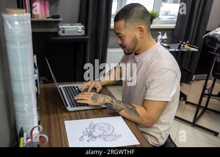 Giovane con tatuaggi che lavora su un notebook Foto Stock
