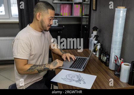Giovane con tatuaggi che lavora su un notebook Foto Stock