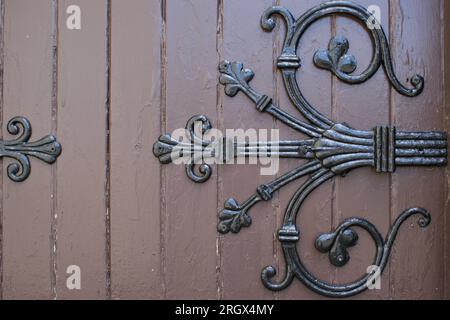 Un frammento di una vecchia porta di legno con un frammento di cerniera decorativa. Vecchia porta della chiesa. Foto Stock