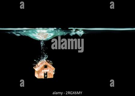 Casa dei giocattoli in miniatura che affonda in acqua su uno sfondo nero con spazio per le copie. Rappresentazione concettuale di sfide inaspettate, avversità o oltre Foto Stock