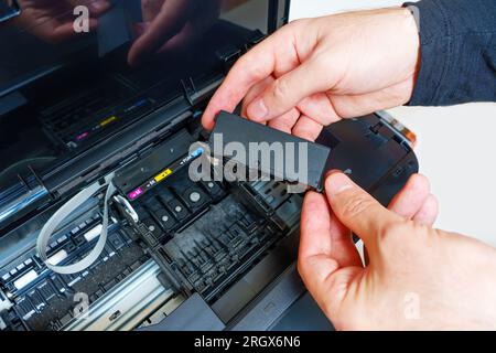 Vista ravvicinata delle mani maschili che tengono una nuova cartuccia d'inchiostro disimballata pronta per essere installata nella stampante a getto d'inchiostro. Foto Stock