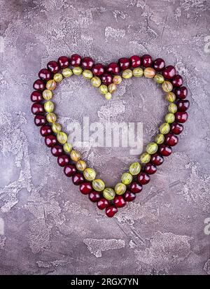 Ciliegie dolci fresche a forma di cuore su sfondo grigio cemento. Vista dall'alto. Spazio di copia. Foto Stock