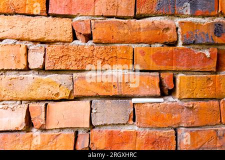 Il gesso della scuola bianca è bloccato in un muro obsoleto e fatiscente di mattoni rossi danneggiati. Foto Stock