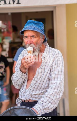 Bell'anziano uomo con gelato in mano. Vecchio con la barba a panama che regge un gelato e sorride. Giornata luminosa e soleggiata nella città di villeggiatura. Foto Stock