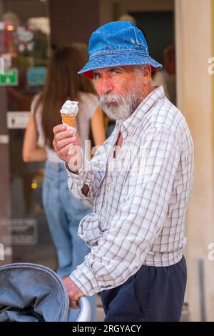 Bell'anziano uomo con gelato in mano. Vecchio con la barba a panama che regge un gelato e sorride. Giornata luminosa e soleggiata nella città di villeggiatura. Foto Stock