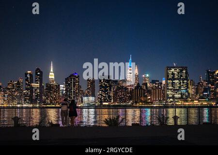 Collegamento Cityscape: Una coppia gode della vista da Hunter's Point, Long Island City, mentre lo skyline di Manhattan illumina la notte sull'East River Foto Stock