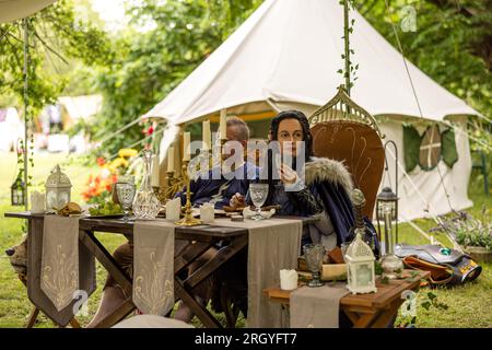 Cottbus, Germania. 12 agosto 2023. I partecipanti all'Elven Forest Festival, che appaiono come hobbit e si accamparono in una tenda dal design elegante durante l'evento, si siedono davanti alla tenda durante una pausa. Il festival è principalmente un raduno per i fan di popolari serie fantasy e fantascientifiche come Harry Potter, Star Wars e il Signore degli anelli. Per il festival di tre giorni, gli organizzatori si aspettano 15000 visitatori di tutte le età provenienti da tutto il paese, che potranno assistere a concerti, workshop e altri eventi. Crediti: Frank Hammerschmidt/dpa/Alamy Live News Foto Stock