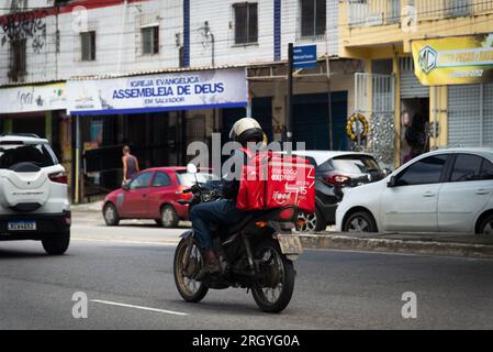 Salvador, Bahia, Brasile - 11 agosto 2023: Un addetto alla consegna di cibo che utilizza l'app ifood viene visto in sella alla sua moto su Avenida Bonoco a Salvador, Bah Foto Stock