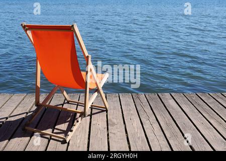sdraio pieghevole vuota sul ponte di legno che si affaccia sul lago di acque calme Foto Stock