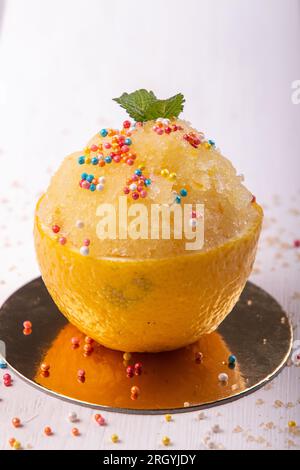 Sorbetto al limone con spolverino pasquale. Dessert estivo rinfrescante a metà buccia di limone su sfondo bianco oro. Foto Stock