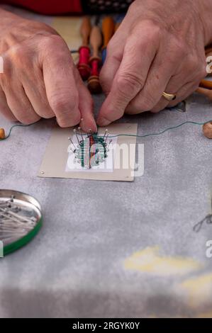 Mani di persone che preparano e preparano il merletto a bobina. Fili di pizzo colorati. Attività ricreative. Foto Stock