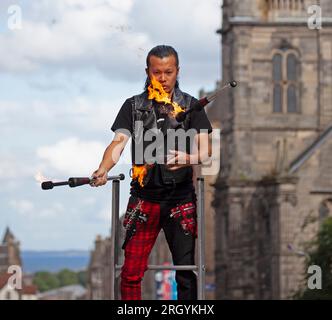 Royal Mile, Edimburgo, Scozia, Regno Unito. 12 agosto 2023. Edinburgh Festival Fringe, artisti di strada di High Street che si esibiscono per un grande pubblico, ventoso per chi si destreggia con il fuoco e sulle piattaforme, il sole e occasionali docce pesanti. Nella foto: Showtime per Kozo Kaos mentre si destreggia con le torce di fuoco nel vento di High Street. Credito: Notizie dal vivo Archwhite/alamy. Foto Stock