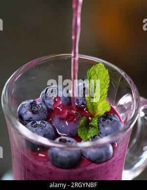 refrigerare per fare gelatina dolce sano aiutare le articolazioni. preparazione della gelatina di mirtilli con gelatina versare un flusso sottile in un bicchiere di vetro Foto Stock