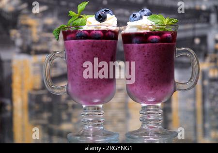 Festa per due dolci in un bicchiere di vetro a due mani prendi un dessert ai mirtilli con menta e vaniglia con panna e mirtilli freschi in direzioni diverse. spazio per la pubblicità di testo Foto Stock
