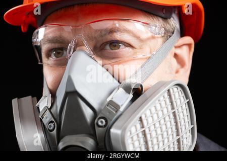 Un uomo che indossa un casco, un respiratore e degli occhiali su sfondo nero Foto Stock