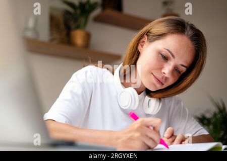 Una giovane studentessa universitaria moderna fa i compiti sedendo alla scrivania a casa. Foto Stock