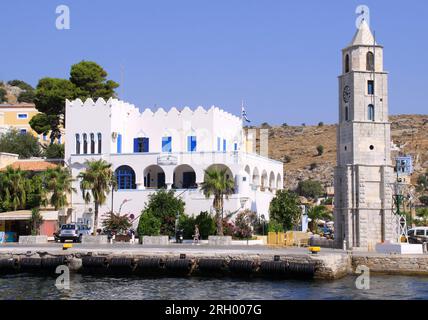 SYMI, GRECIA - 14 LUGLIO: Donna non identificata che cammina accanto all'edificio della stazione di polizia ellenica e alla torre dell'orologio al porto. Luglio 14,2013 a Symi, Grecia Foto Stock