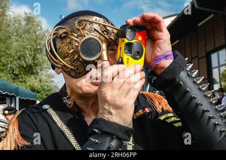 Henrichenburg, Waltrop, Germania. 12 agosto 2023. Un fan dello steampunk cerca di scattare foto con i suoi occhiali monoclici. Gli appassionati di steampunk, i gruppi in costumi e i visitatori, molti in abiti retrò-futuristici o di ispirazione vittoriana, si divertono nonostante le forti docce a pioggia del primo giorno del weekend del Festival del Giubileo di Steampunk presso lo storico skilift di Henrichenburg, un monumento architettonico e sito del patrimonio industriale. Crediti: Imageplotter/Alamy Live News Foto Stock